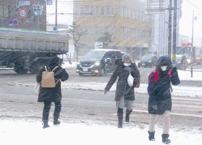 写真：横殴りの雪の中、フードを深くかぶり通勤通学する市民ら＝１５日午前８時１５分ごろ、室蘭市東町