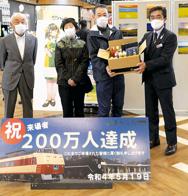 写真：２００万人目の記念として及川町長から道の駅製品詰め合わせを受け取る真柄さん夫婦（中央）