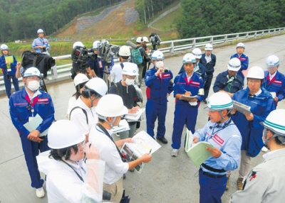 写真：報道陣に厚真ダムの復旧状況を説明する道開発局職員（手前右）。のり面工事（後方）などを終え、来年度から供用開始を予定している