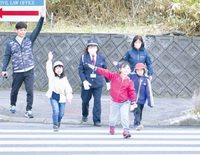 写真：指導員と一緒に大きく手を上げて横断歩道を渡る児童たち