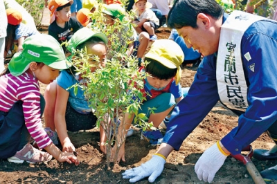 写真：ツツジの苗木を植える子どもたちと市長（右）