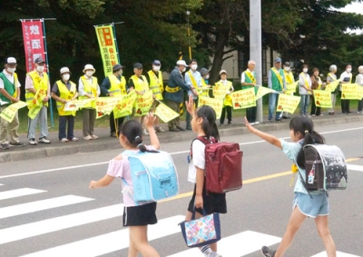 写真：青葉小前の横断歩道を渡る児童を見守る参加者たち