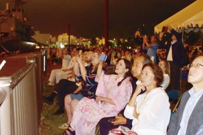 写真：スマートフォンを手に花火を観賞する室蘭商工会議所の招待客たち＝２６日午後９時、室蘭港中央ふ頭