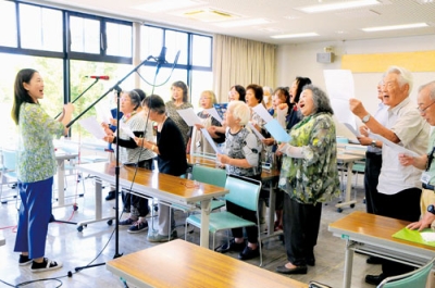 写真：完成した長生大学校歌を練習する学生たちと太田さん（左）