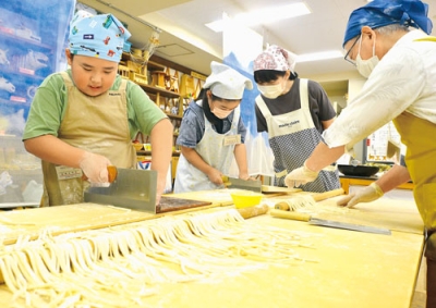 写真：大きな包丁でうどんの生地を丁寧に切る参加者たち