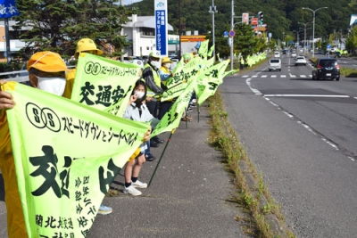 写真：黄色い交通安全旗を掲げドライバーに安全運転を呼びかける参加者