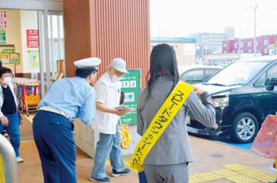 写真：買い物客に啓発物を渡す藤田登別交番所長