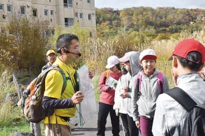 写真：阿部代表理事のガイドで、２０００年噴火の爪痕が色濃く残る旧桜ヶ丘団地を見学する児童たち