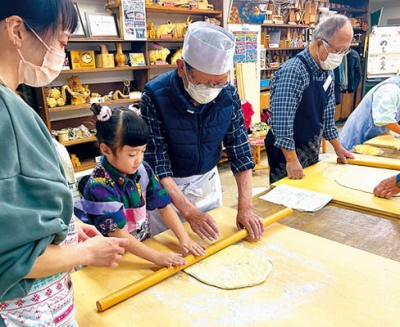 写真：麺棒を使いスタッフと一緒に生地を伸ばす参加者