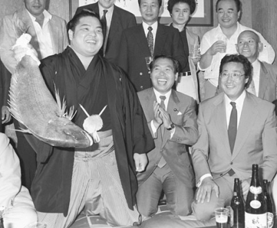 写真：１９８７年９月、大相撲秋場所で優勝しタイを手に笑顔の横綱北勝海（現八角理事長）。右端は師匠の北の富士勝昭さん＝東京都墨田区