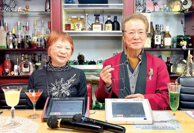 写真：自作の知恵の輪を手に来店を呼びかけるマスターの鈴木英秋さんとママの三津枝さん