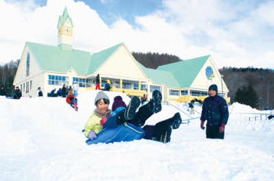 写真：雪の滑り台を上手に滑り、笑顔を見せる子どもたち