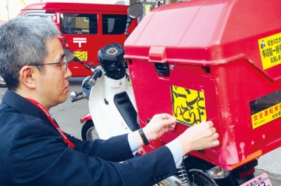 写真：バイクにステッカーを貼り付ける室蘭郵便局の山田局長