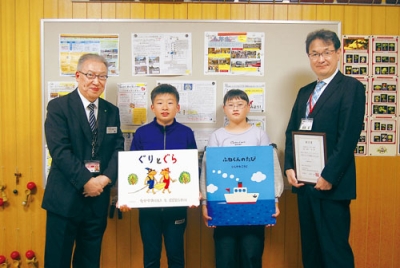 写真:川上参事(左)から図書や贈呈書を受け取った児童代表と萩原校長