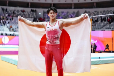 写真:体操の世界選手権男子個人総合で3連覇を果たし、日の丸を掲げる橋本大輝=22日、ジャカルタ(共同)