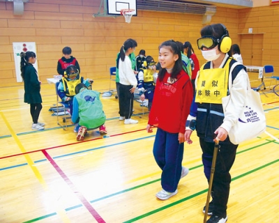 写真:ゴーグルやサポーターを装着し、高齢者の日常動作を疑似体験する児童