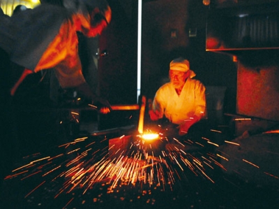 写真:赤く熱した玉鋼を打つ刀匠ら