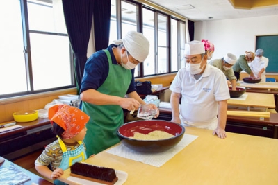 写真:アドバイスを受けながらそば打ちに挑戦する参加者