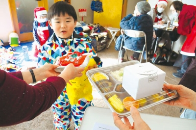 写真:Xマスメニューの弁当とケーキを受け取る子