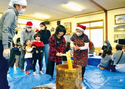 写真:サンタの帽子をかぶった町内会関係者に見守られながら、餅つきを楽しむ子どもたち