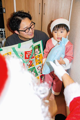 写真:突然のサンタ登場に驚きながらプレゼントをもらう子ども=24日午後5時50分ごろ、豊浦町