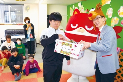 写真:にゃんまると吉田店長(右)から菓子を受け取る子どもたち=放課後等デイサービスほくと