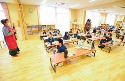 写真:對馬理事長(左)から料理やかえる食堂について説明を受ける児童ら