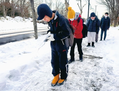 写真:滑り止めの砂を歩道にまく生徒たち