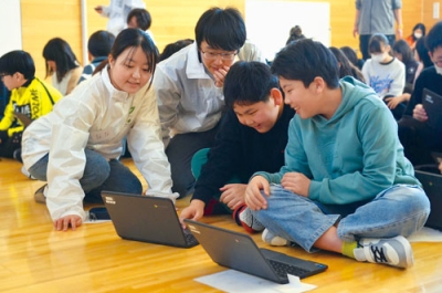 写真:サポート役の大学生から説明を受けながらプログラミングに挑戦する児童