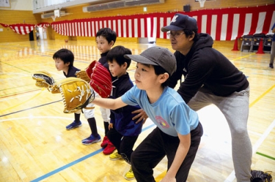 写真:大谷選手が寄贈したグラブを着用し、本間監督(右)の指導を受ける選手たち